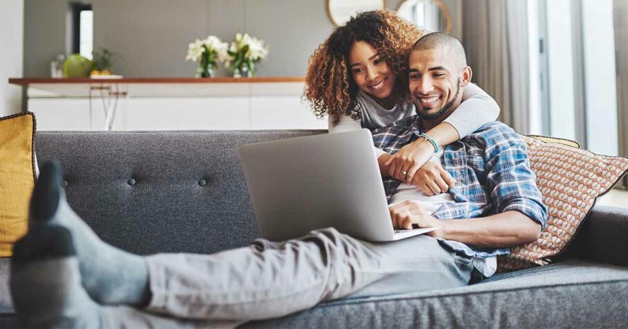 Young couple in their 30s looking at a laptop while relaxing on a couch