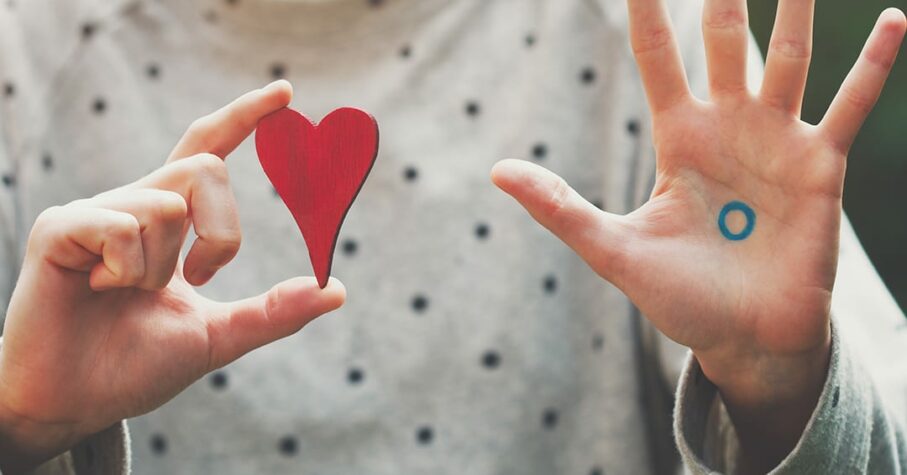 girl holding a heart shape on right hand and showing the blue circle with palm open on the left hand