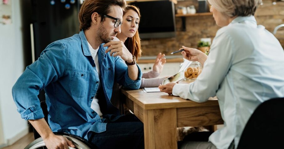 man on a wheelchair with his wife deciding for a critical illness insurance with an advisor