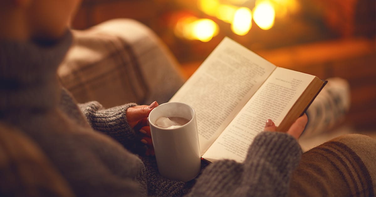 woman reading a book with a hot coco on a warm cozy environment