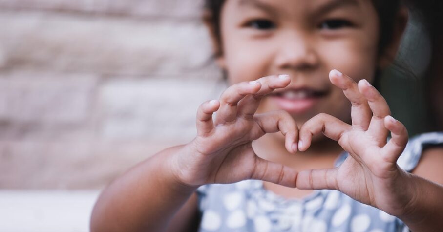 Asian kid doing heart shape with hand