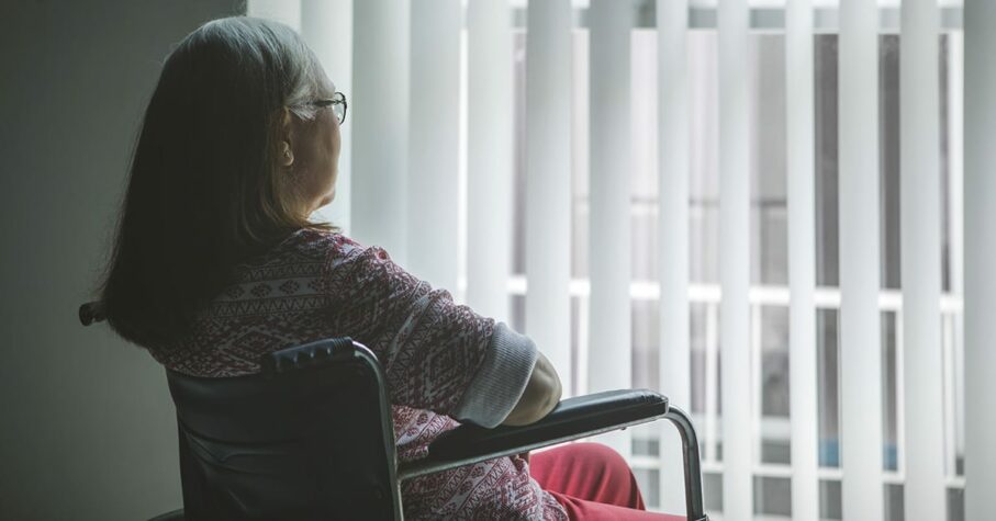 Old woman with stroke on a wheelchair looking out the window