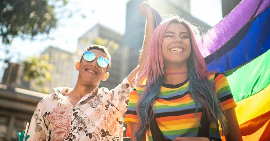 a woman in rainbow shirt and a man holding the pride flag on pride parade