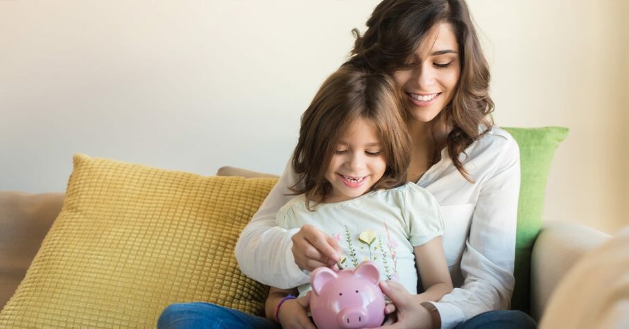Mother and Daughter on the couch putting coin a pink piggy bank
