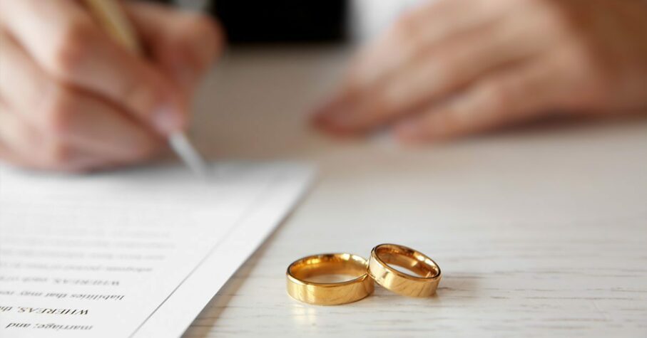 Signing a prenuptial agreement with gold wedding rings on the table