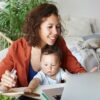 woman working at desk at home using laptop, holding baby on her lap