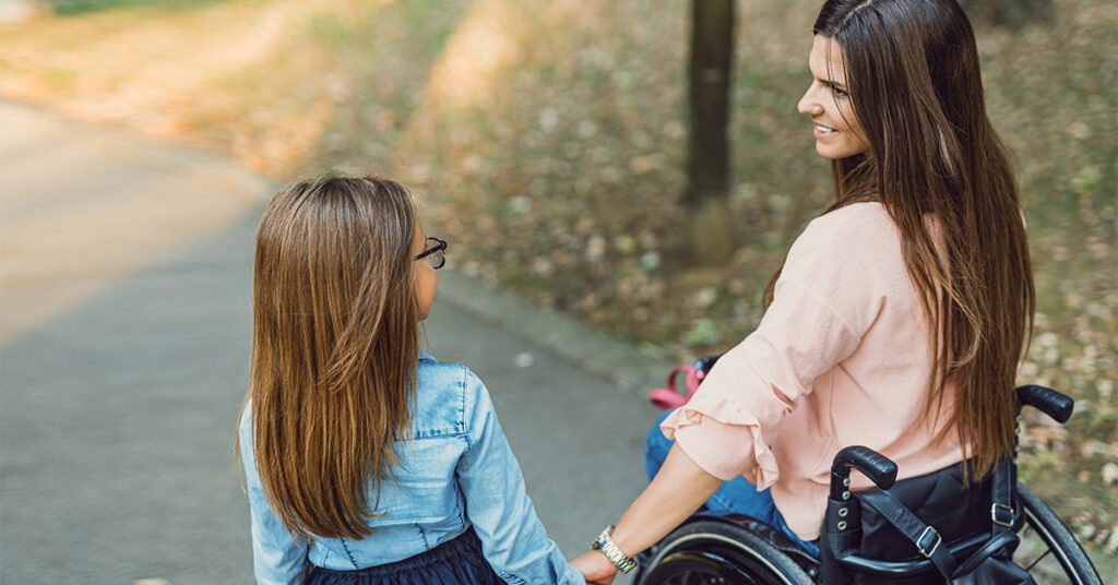 Mother in a wheelchair holding the hand of her daughter in the park