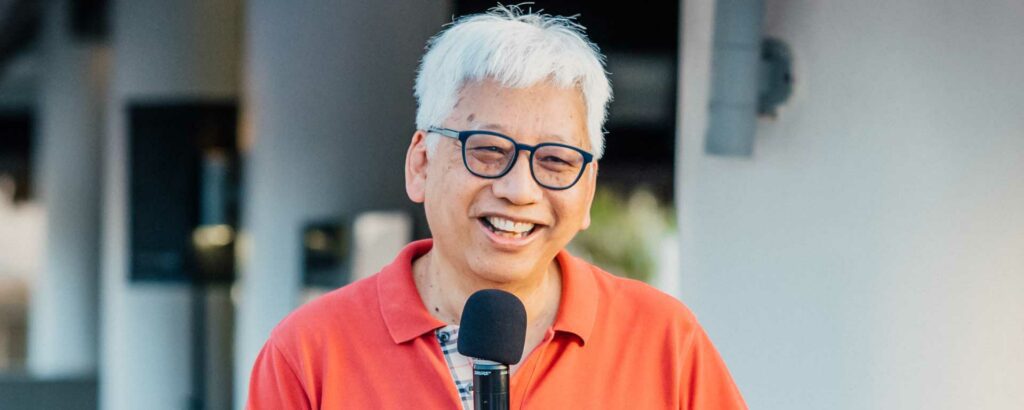 Henry Auyeung holding a microphone talking to an audience