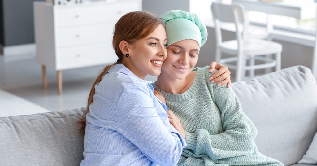 woman hugging a female friend with ovarian cancer in the couch.