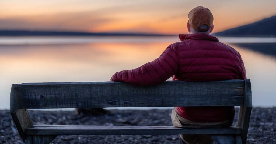 back of man sitting on bench looking out at the lake